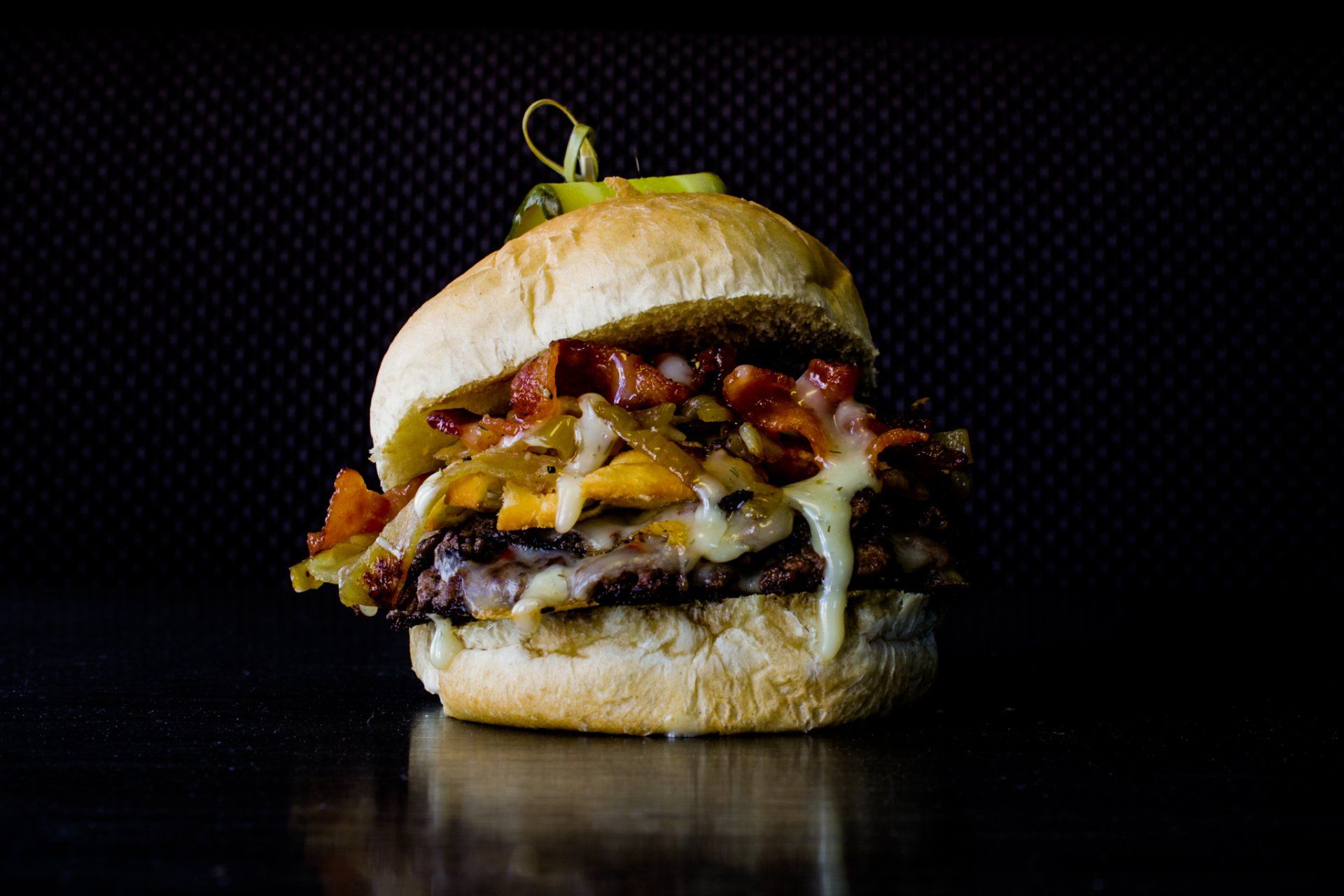 Close-up of a stacked cheeseburger with bacon, sauce, and melted cheese on a dark background