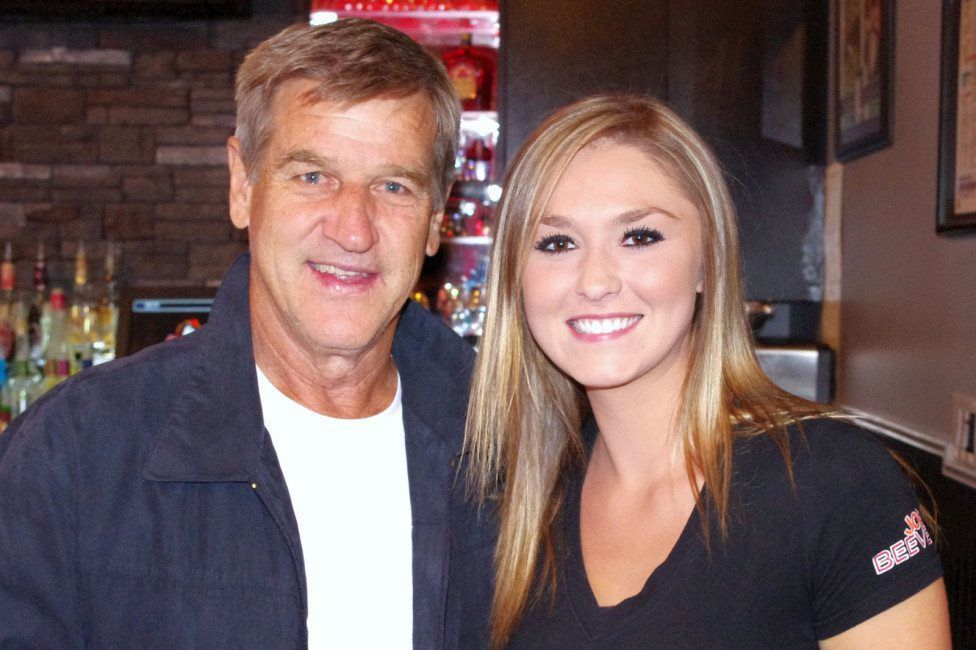 Two people smiling indoors at a restaurant, standing close together.