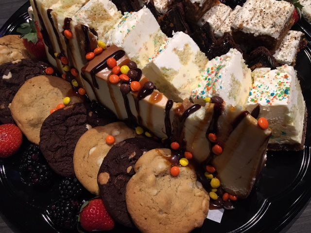 Dessert platter with cookie slices, brownies, strawberries, and chocolate drizzle on a black tray