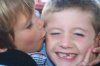 Woman kissing a smiling child’s cheek, close-up outdoors.