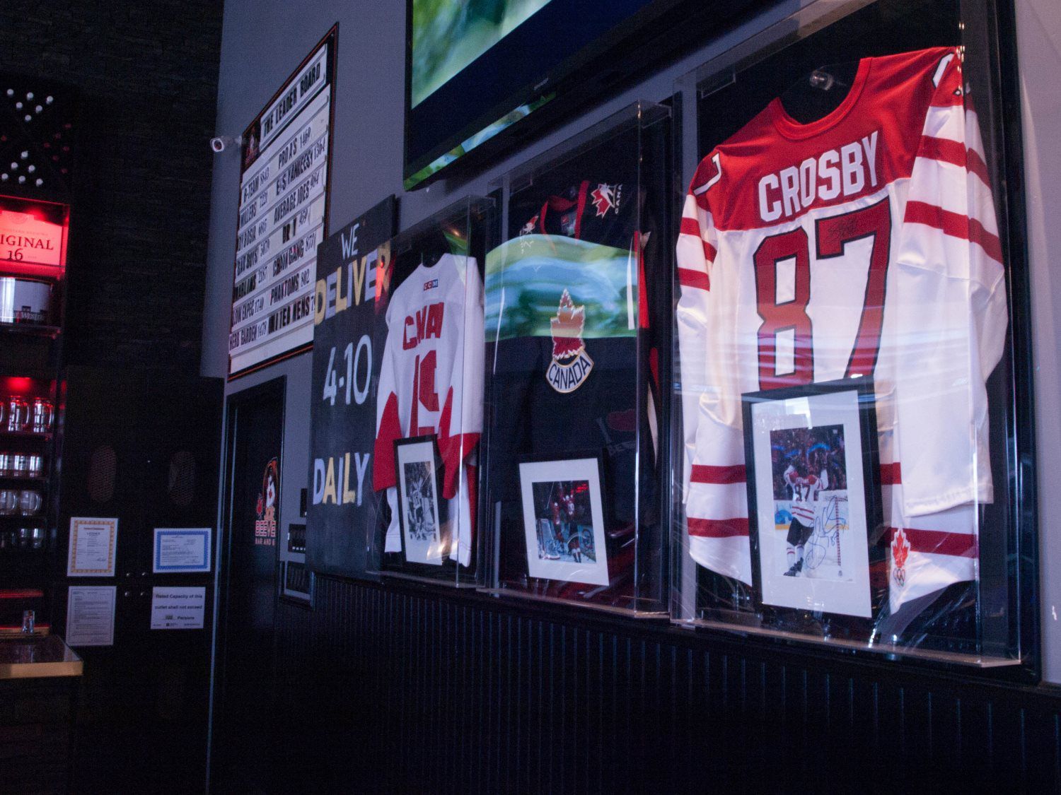 Sports bar display with framed hockey jerseys, including a red Crosby 87 jersey, behind glass.