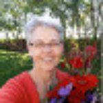 Smiling person in a red sweater standing outdoors near red flowers and greenery