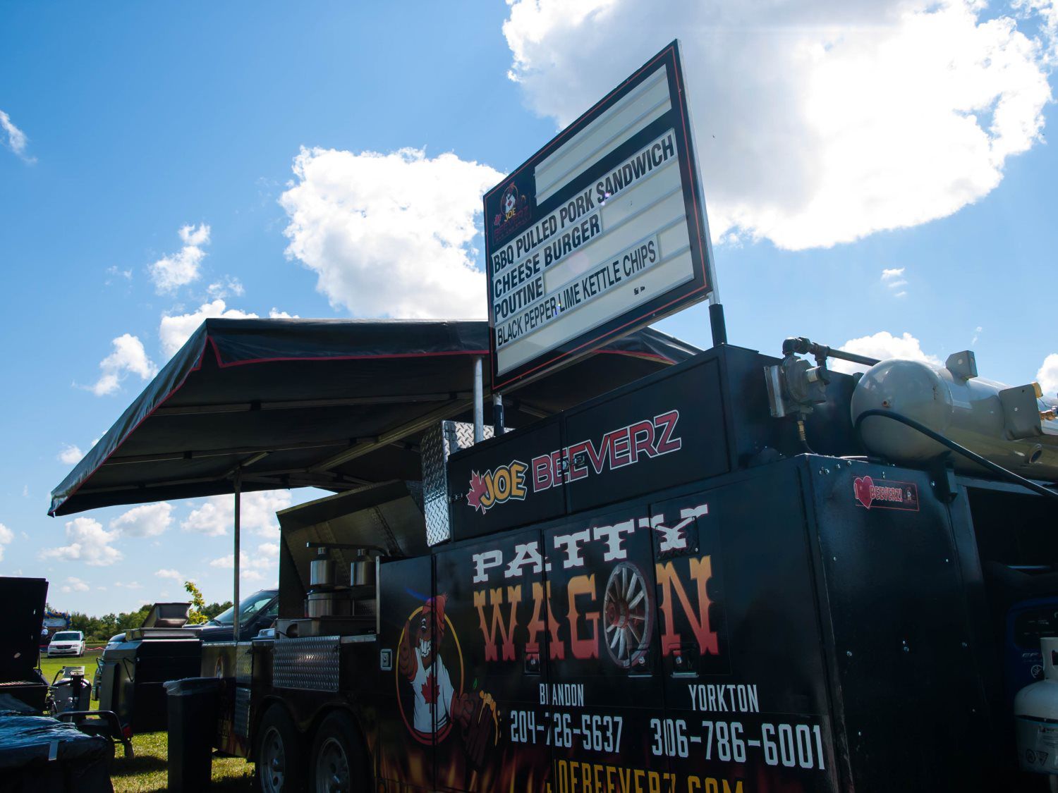 Food truck under a canopy with a large “Patti Wagon” sign against a bright blue sky.