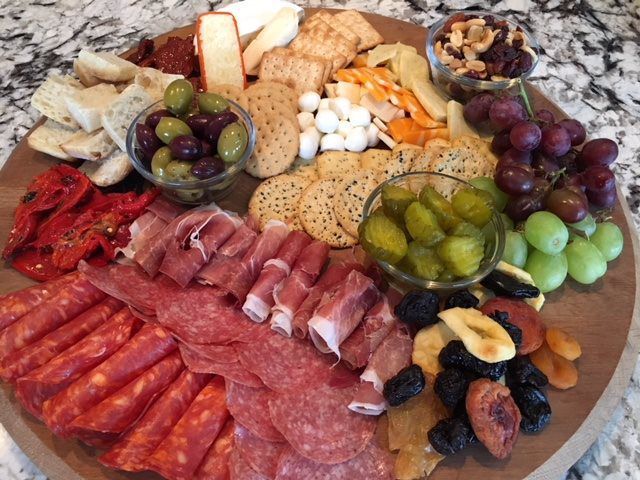 Charcuterie board with assorted cheeses, meats, crackers, grapes, olives, nuts, and dried fruit