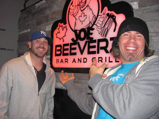 Two men smiling and posing with a Joe Beaver Bar and Grill sign at night