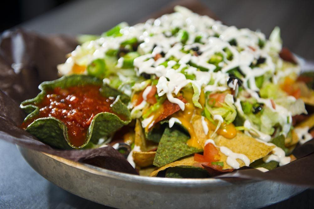 Nachos topped with shredded cheese, salsa, and avocado in a dark bowl