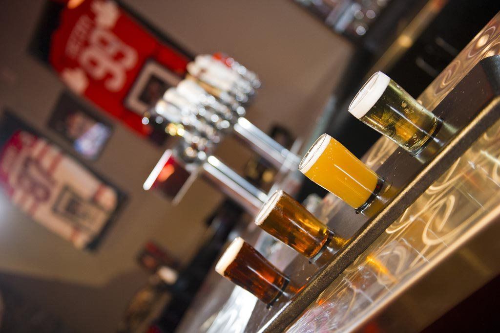 Three glasses of beer on a bar counter in a warmly lit pub