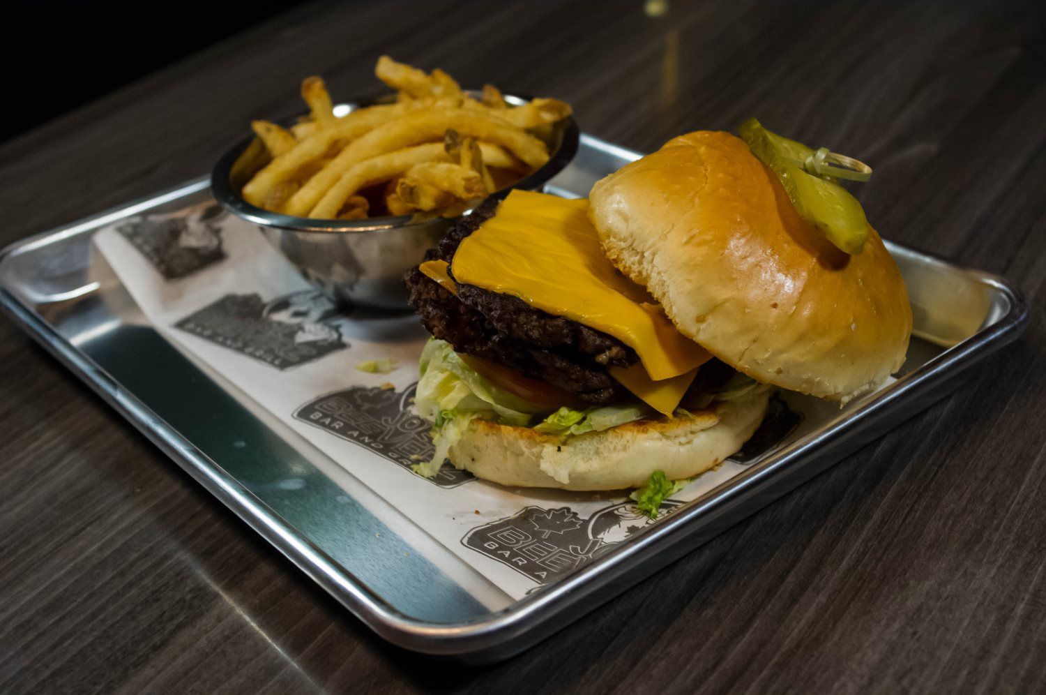 Cheeseburger and fries on a tray, with a napkin on a dark table.