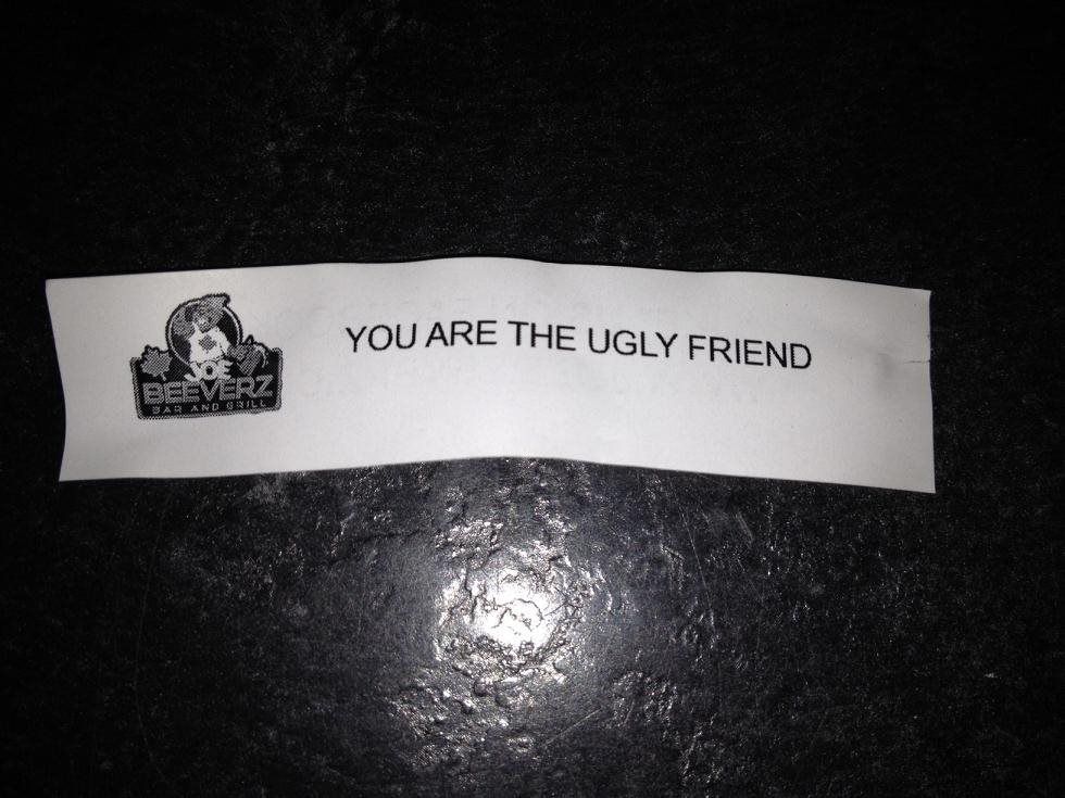 Small white paper strip on a dark surface reading “YOU ARE THE UGLY FRIEND.”