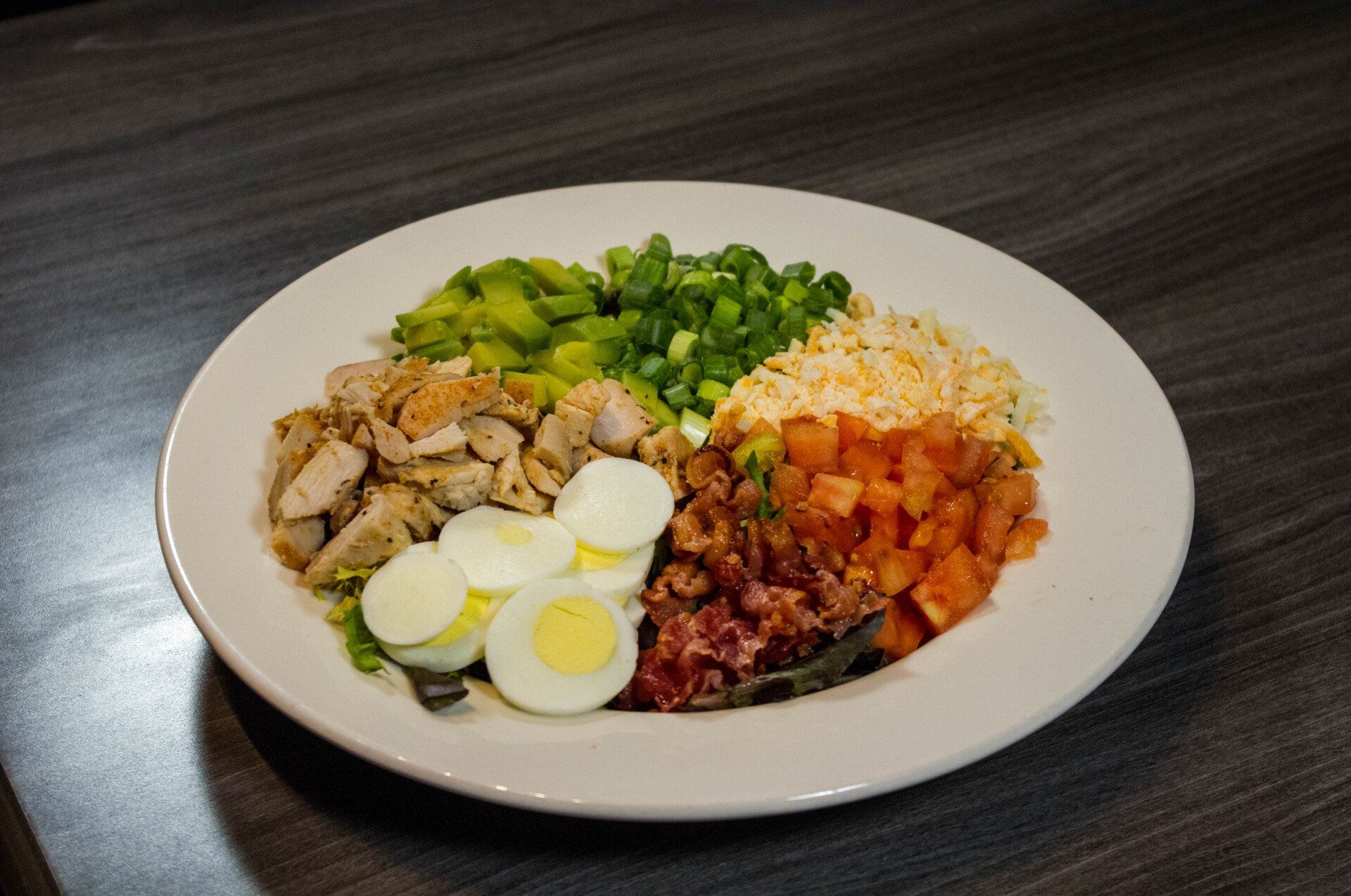 Plate of rice with sliced eggs, chopped green vegetables, and saucy meat on a table