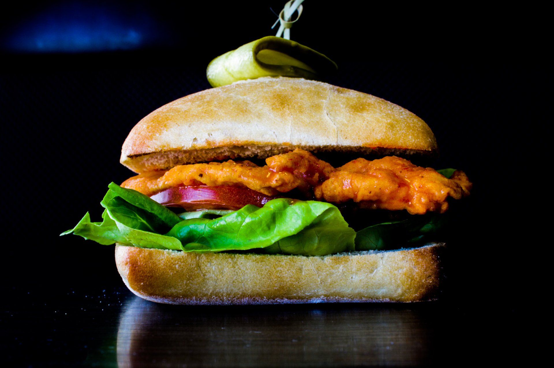 Close-up of a chicken sandwich with lettuce, onion, and a pickle on a dark background
