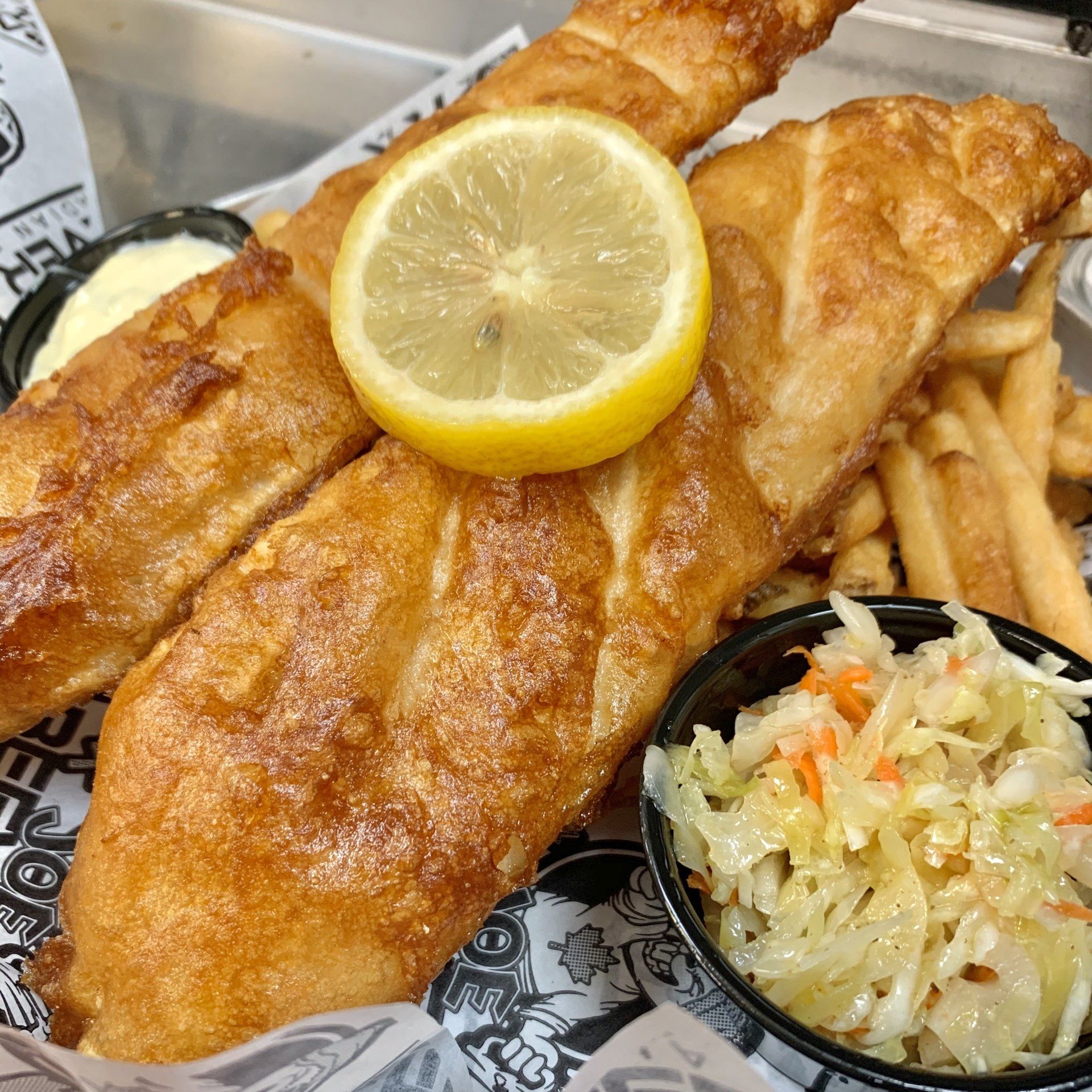 Fried fish and chips with lemon wedge and coleslaw in a takeout basket