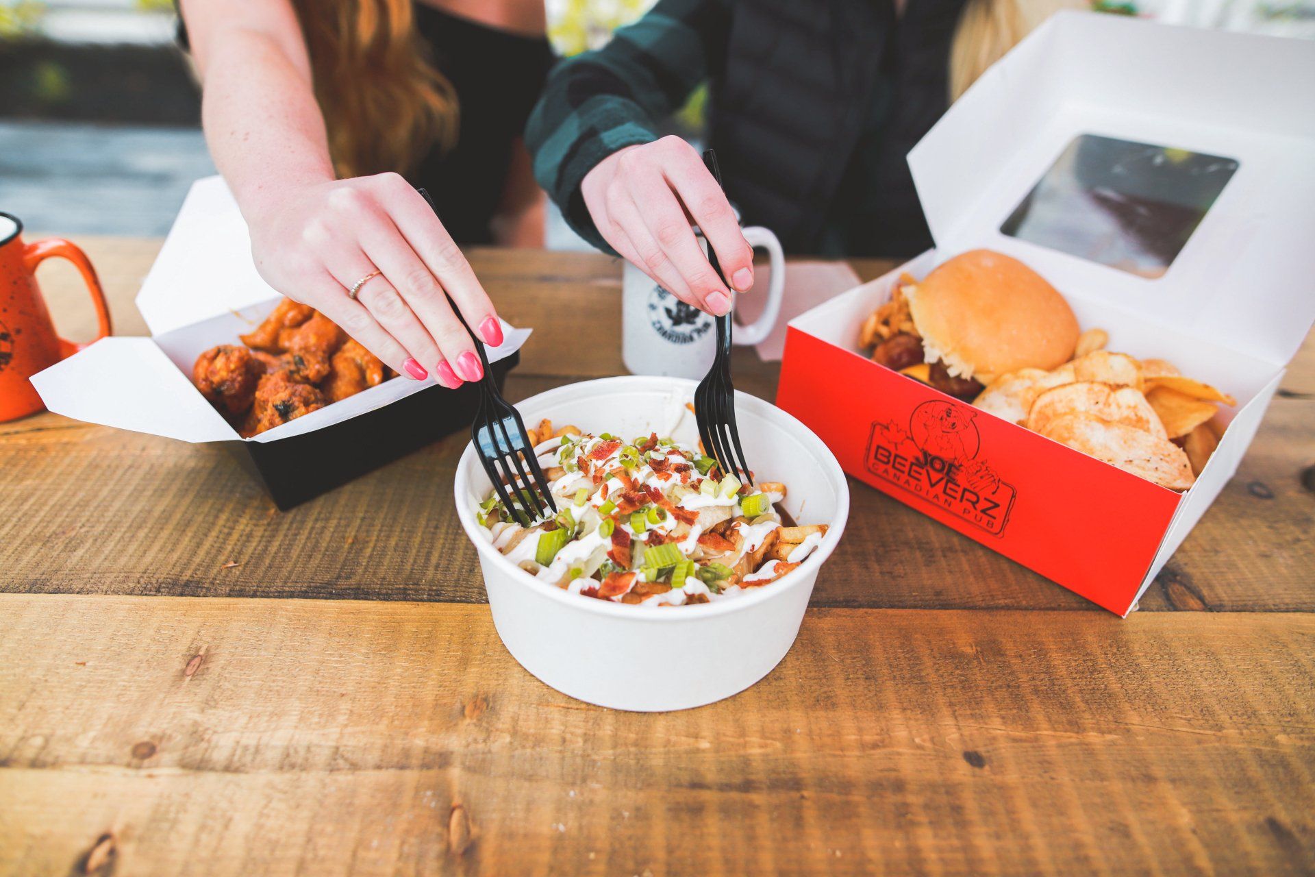 Hands serving fast food and salad on a wooden table at a casual dining setup