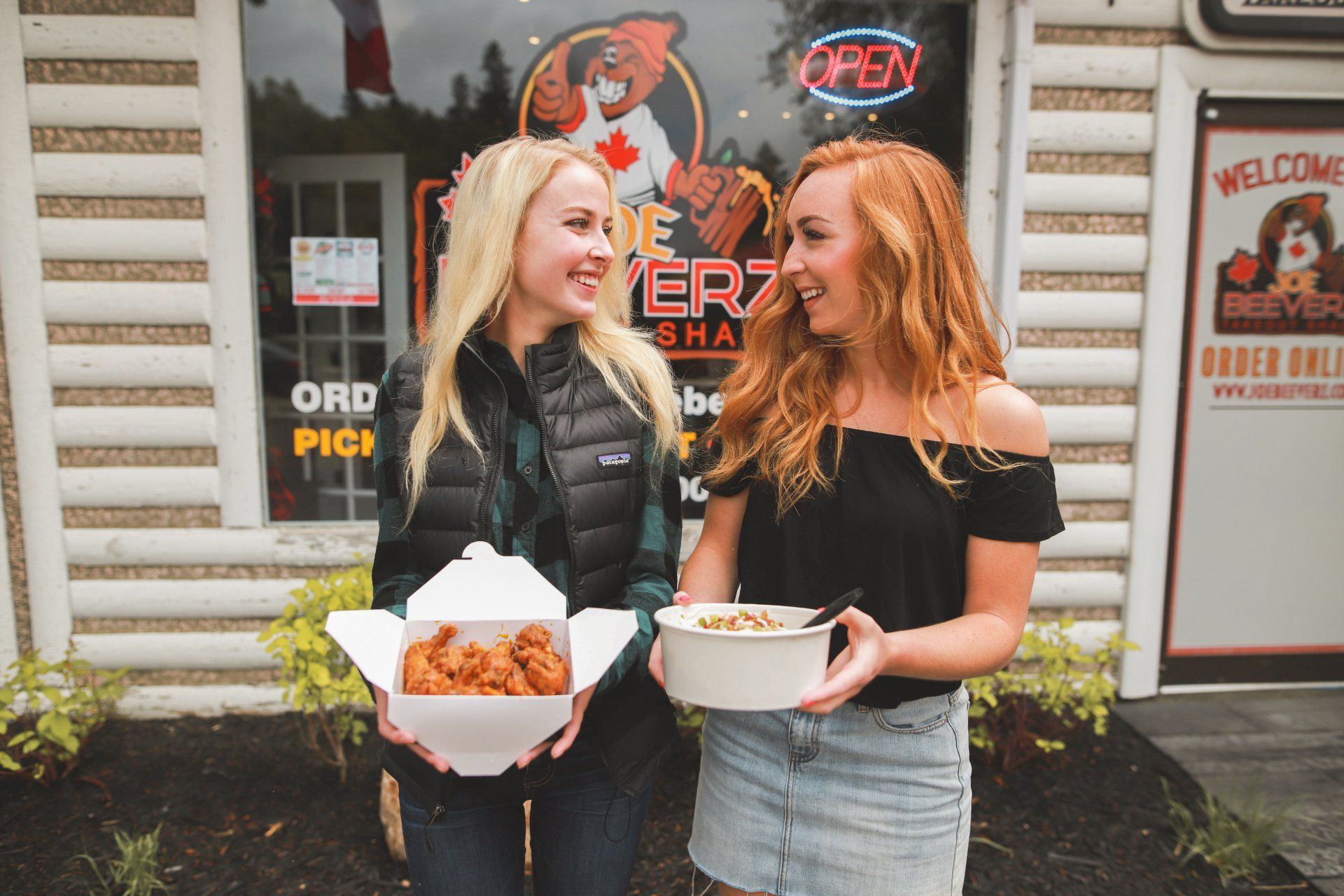 Two women holding takeout boxes and bowls of food outside a shop