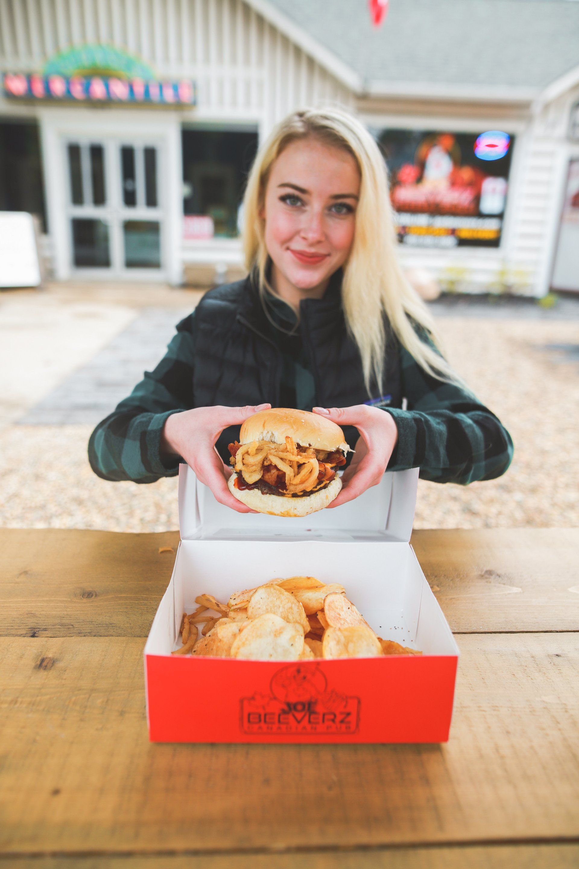 Woman holding a burger over a box at an outdoor table; restaurant entrance in the background