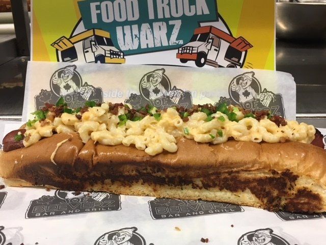 Large hot dog topped with macaroni and peas at a Food Truck Wars event