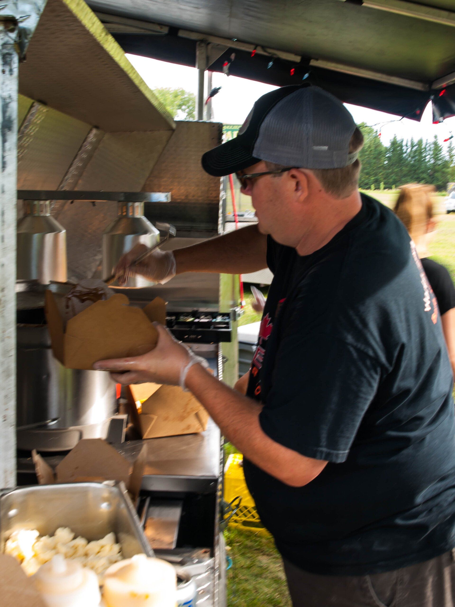Vendor scooping food into a brown paper container at an outdoor concession stand