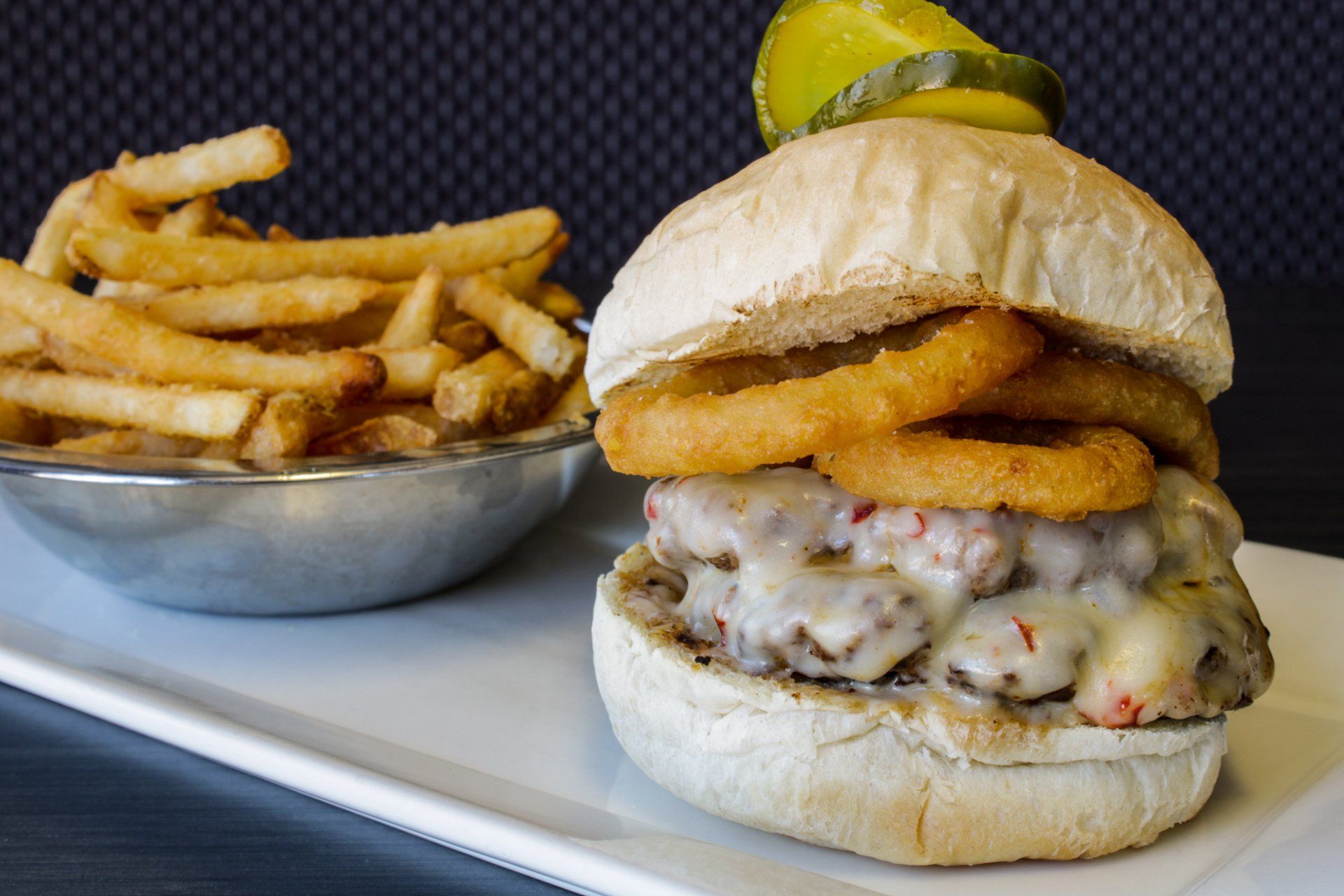 Burger with onion rings and fries on a white plate, with a lemon wedge in the background