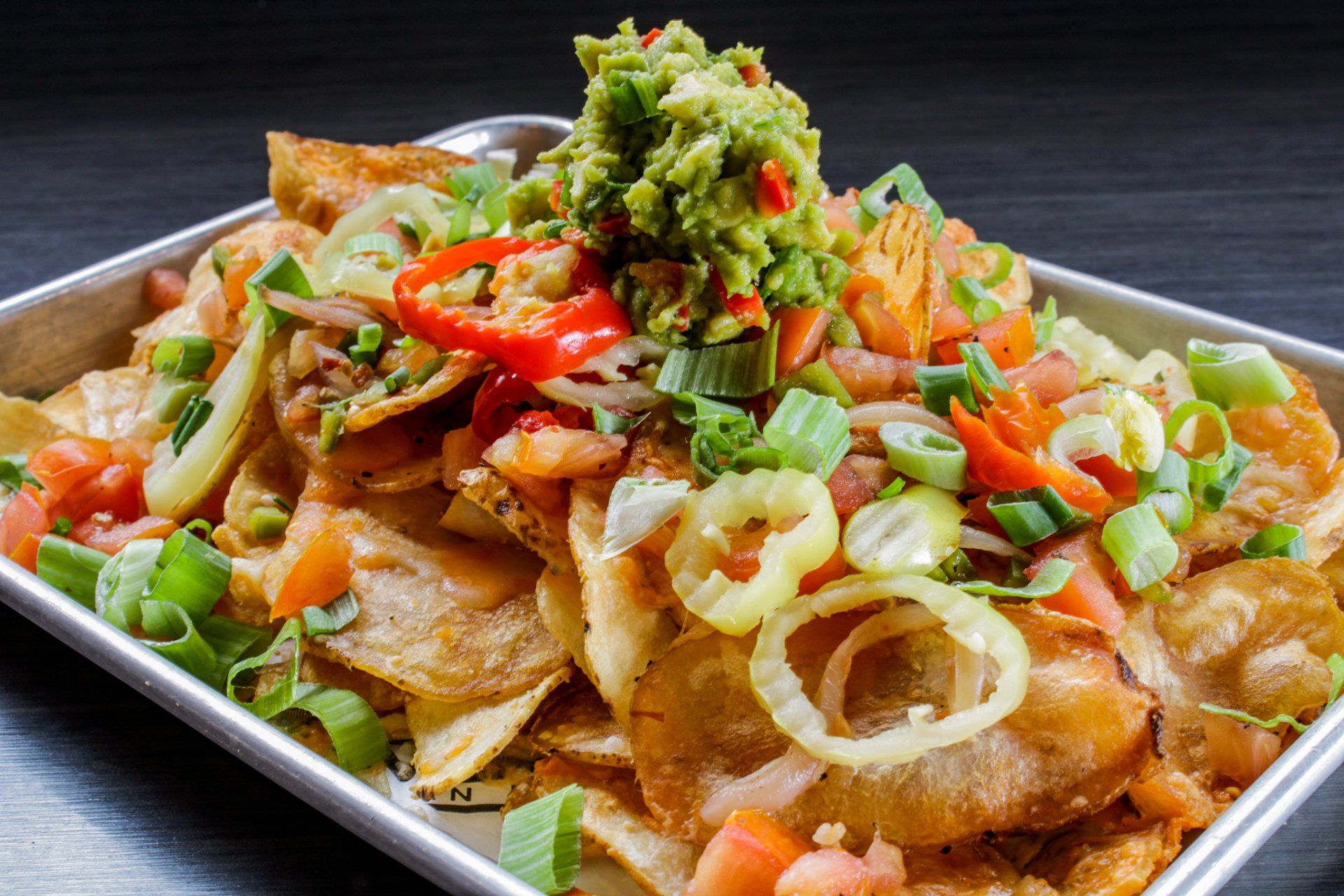 Loaded tortilla chips topped with salsa, cheese, onions, and green guacamole on a platter