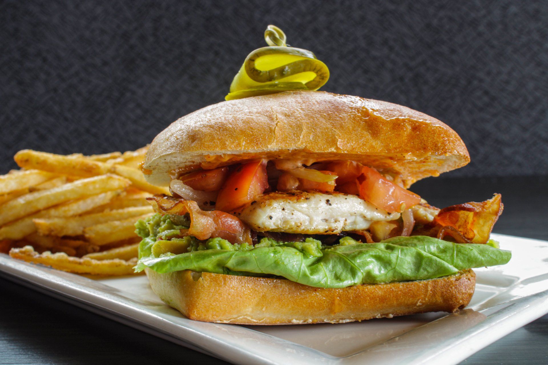 Grilled burger with lettuce, fries, and a green pepper on a white plate