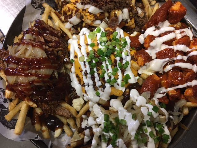 Loaded fries topped with barbecue sauce, cheese, ranch, and green onions in a takeaway container