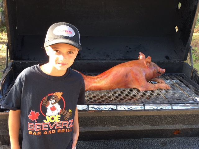 Child standing beside a pig roasting on a grill outdoors
