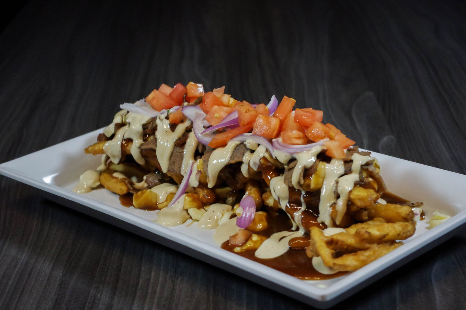 Loaded fries topped with melted cheese, sauce, diced tomatoes, and red onions on a white plate