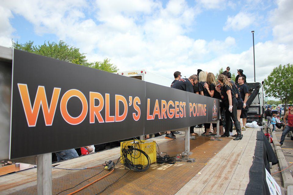 People posing beside a huge “WORLD’S LARGEST…” sign on an outdoor stage
