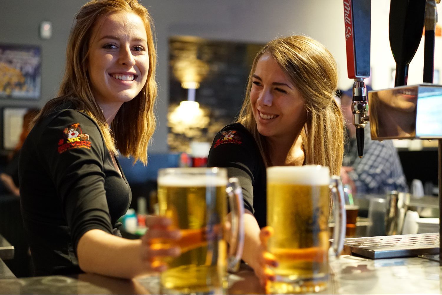 Two smiling women sitting at a bar with drinks in front of them