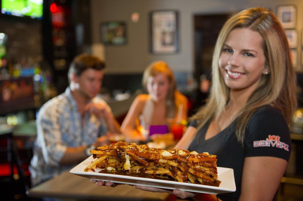 Server holding a tray of fries in a casual restaurant, with diners blurred in the background.