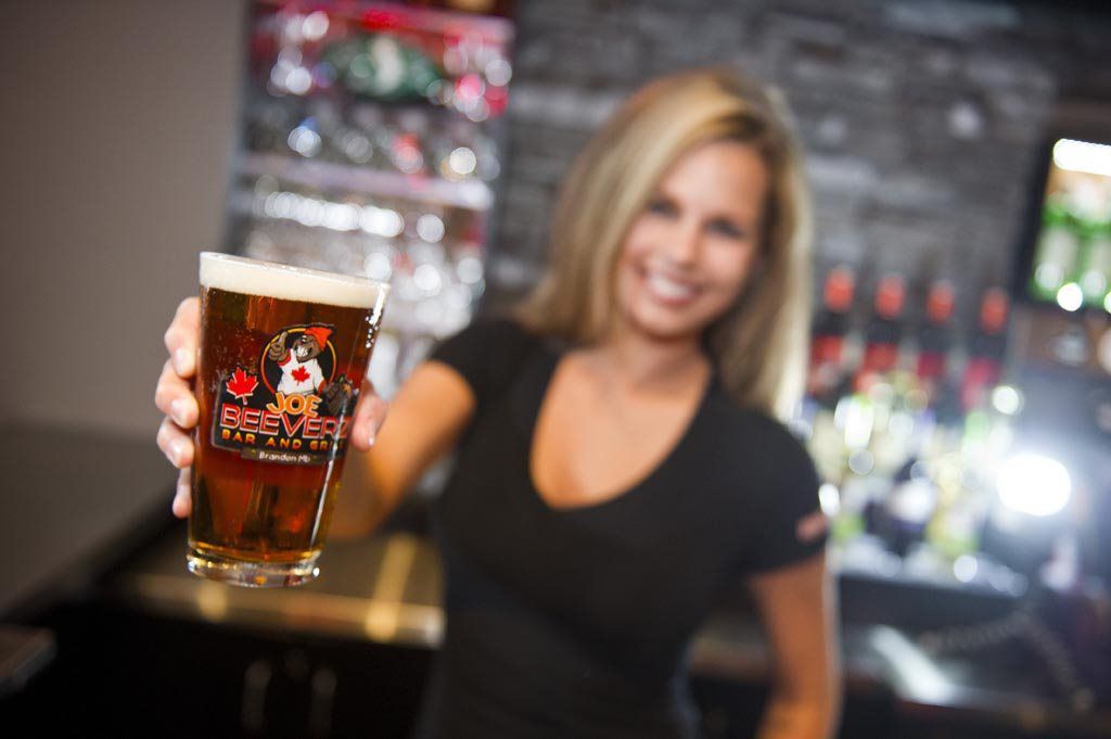 Woman behind a bar holding up a pint of beer with a smile