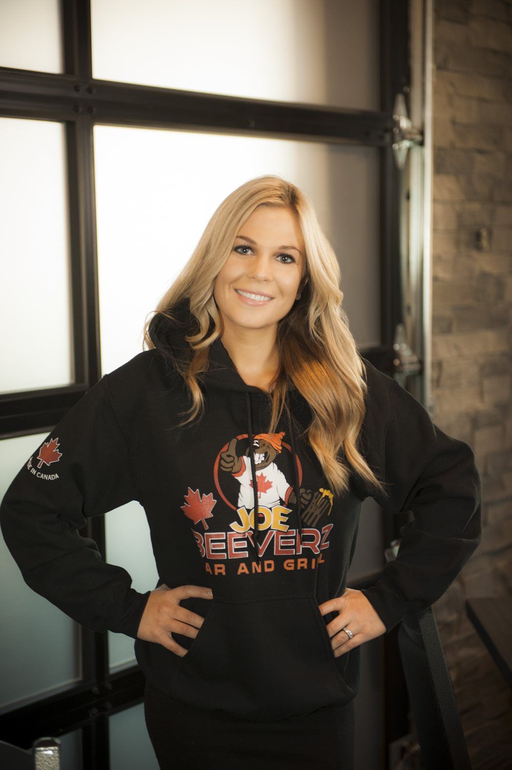 Smiling woman in a black hoodie standing indoors by a window
