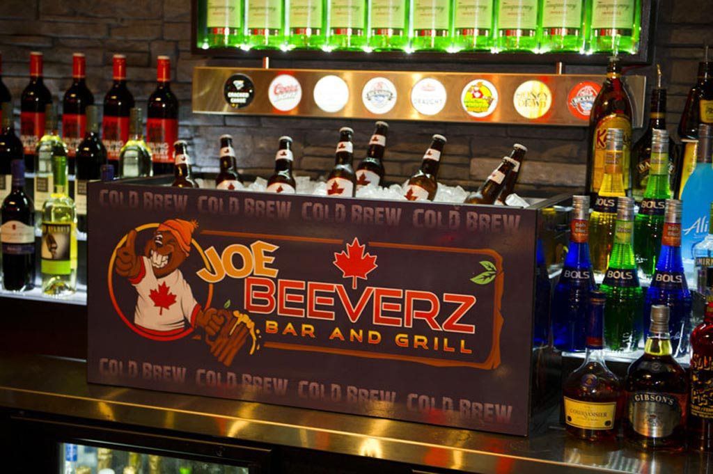 Bar with bottles and illuminated taps behind a “Beeverz Bar and Grill” sign