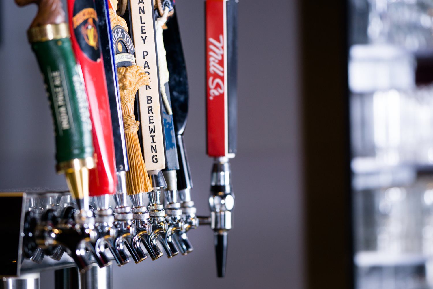Row of colorful beer tap handles with metal spouts in a bar