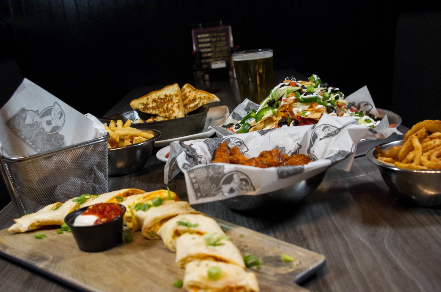 Assorted fried appetizers and wraps on a table, with dipping sauce and salads in a dimly lit restaurant setting