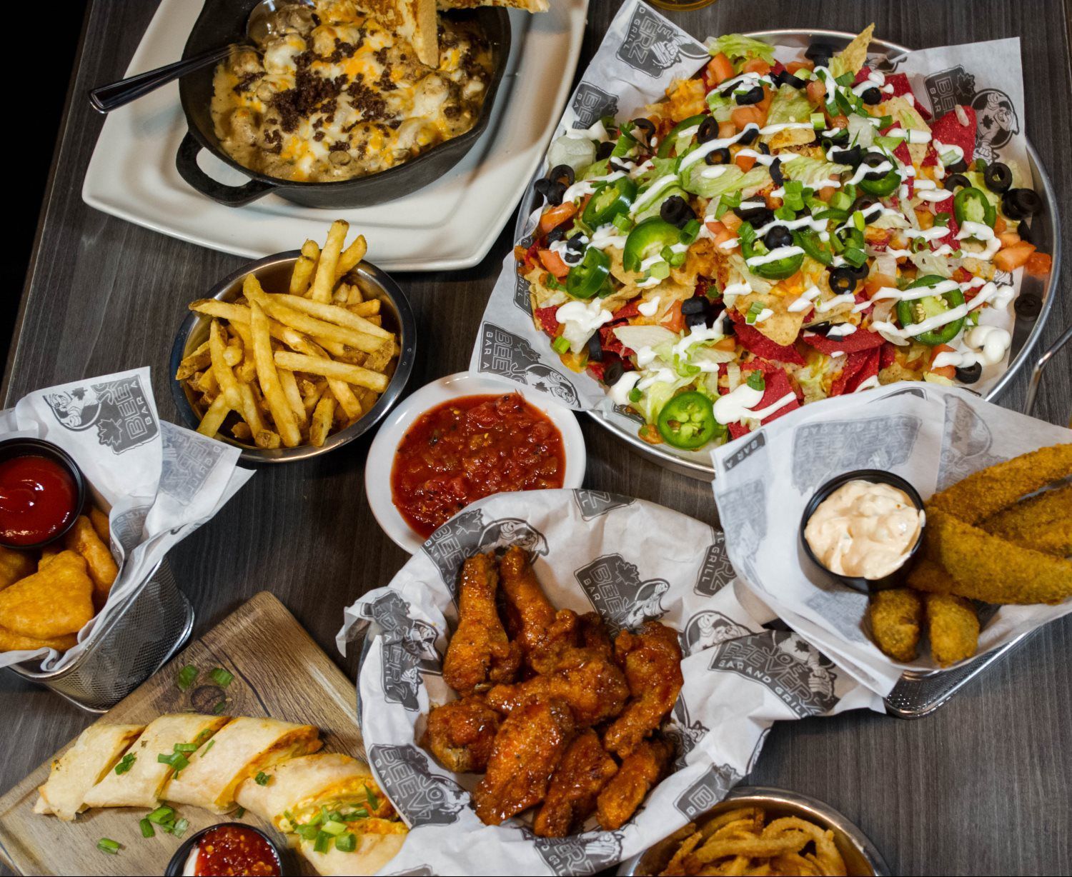 Assorted fried appetizers, fries, and a large salad spread on a table with dipping sauces