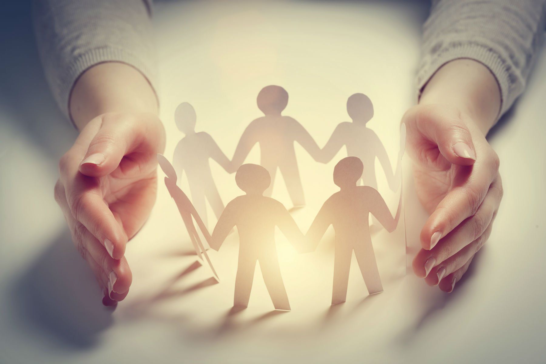 Paper people surrounded by hands in gesture of protection