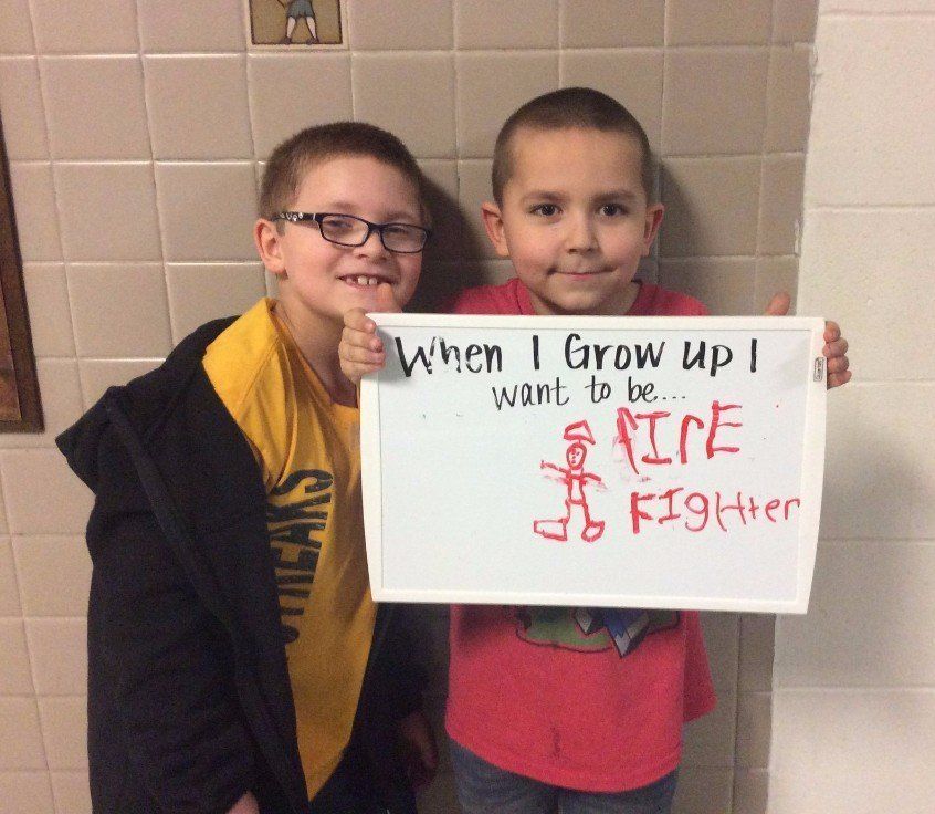 Two young boys holding an artboard that says When I grow up I want to be a fire fighter