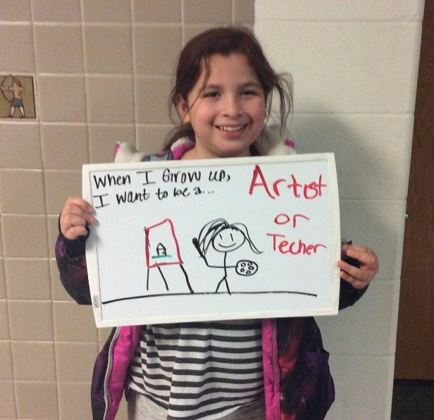 Girl holding an artboard that says When I grow up, I want to be a artist or teacher