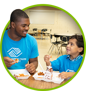 A man and a boy wearing blue Boys & Girls Club of Lenawee shirts having lunch together
