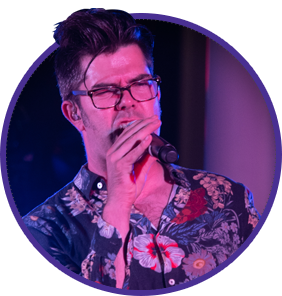 A man wearing glasses is singing into a microphone