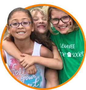 A girl wearing a Lenawee Humane Society shirt is hugging two other girls