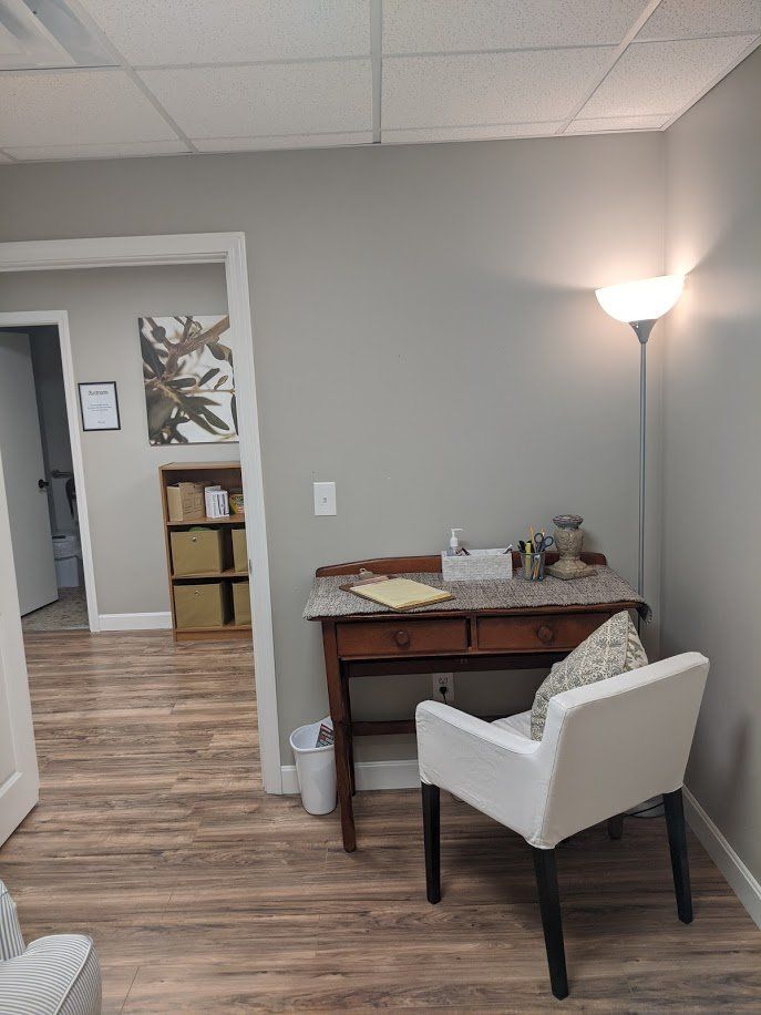 Small waiting area with a white chair, side table, floor lamp, and hallway to a room with boxes.