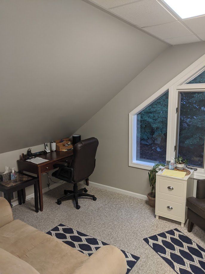 Small attic office with desk, chair, patterned rug, and window by sloped ceiling.