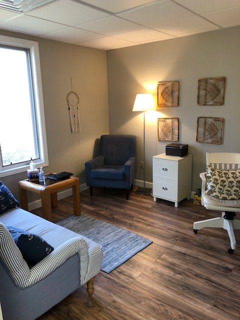 Small living room with blue chair, armchair, lamp, side table, wall art, and wood floor.