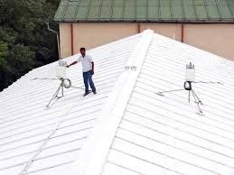 Person on a white roof with two scientific instruments set up on tripods; building in background.