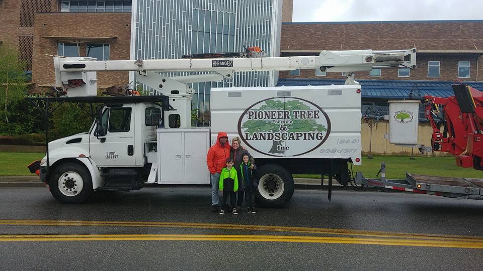 Family poses with a landscaping truck in front of a building.
