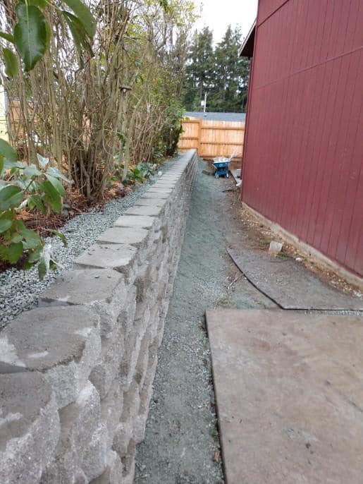Stone retaining wall beside a red building with a gravel path in between.