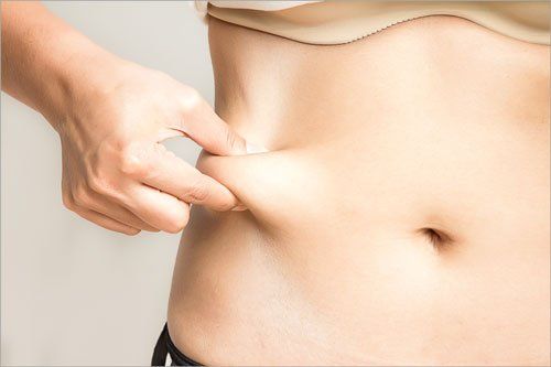 Woman measuring her belly fat with her hands close up