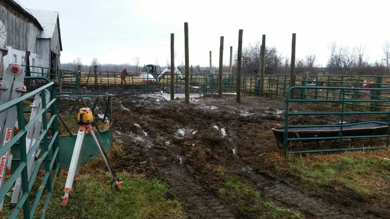 A tripod is sitting in the middle of a muddy field next to a fence.